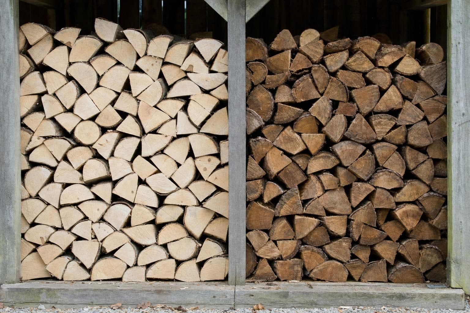 Two stacks of split hardwood logs, one kiln dried and pale, one seasoned and darker